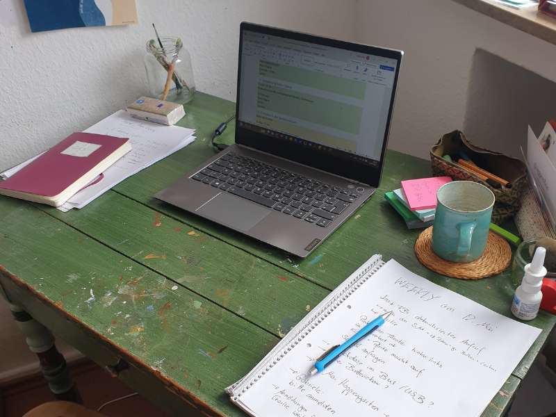 Mein Schreibtisch mit Laptop, Teetasse und Zetteln.