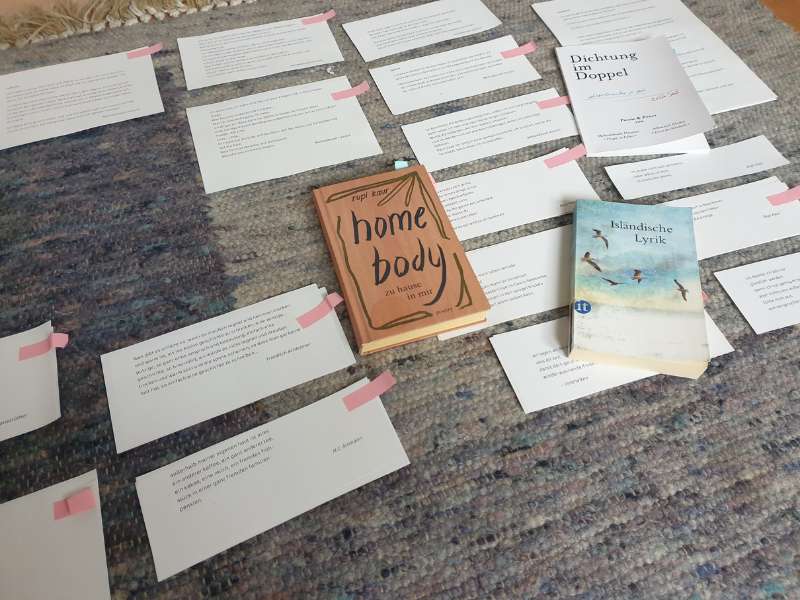 Auf einem blaugrauen Teppich liegen viele Zettel und drei Bücher: "Home Body", "Isländische Lyrik" und "Dichtung im Doppel".