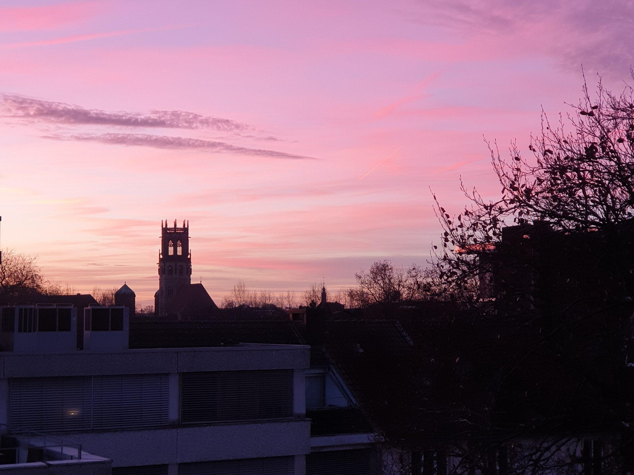 Ein lilafarbener Abendhimmel, ein Baum und ein Kirchturm zeichnen sich dunkel ab.
