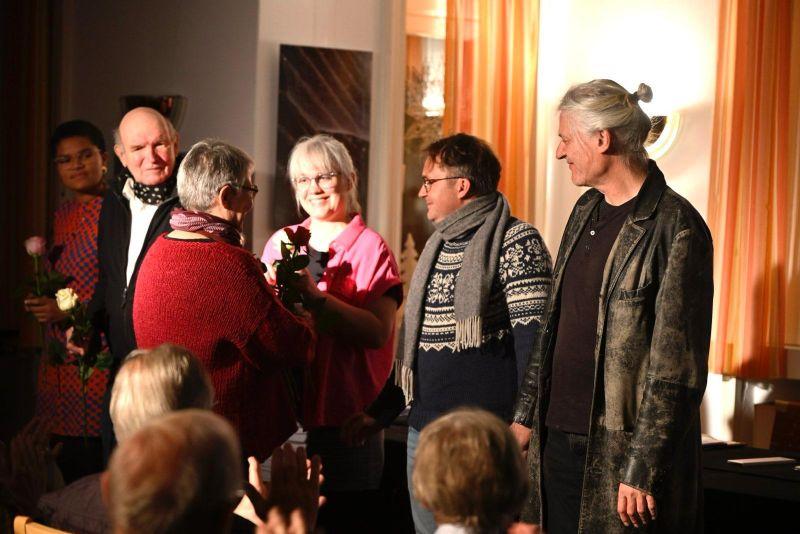Gehen und Ausgehen. Ein Remix nach Thomas Bernhard und Barbi Markovic. Szenische Lesung mit Hartmann & Konsorten, Münster 2025. Foto: Martin Breutmann Fünf Menschen stehen in einer Reihe und bekommen Blumen überreicht.