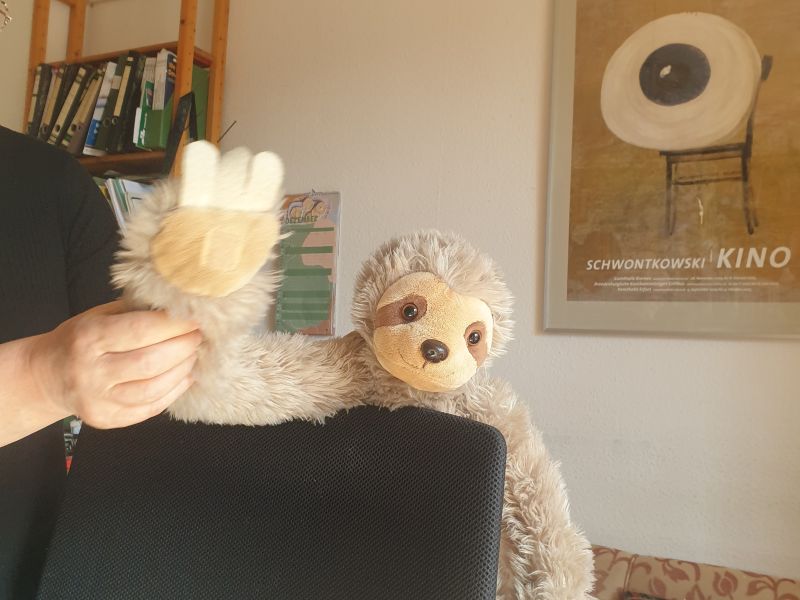 Ein Stoff-Fautier, das über eine Stuhllehne schaut und winkt.