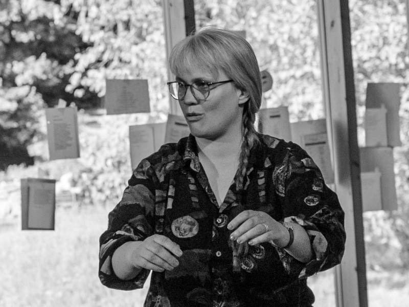 Paula Marie Berdrow by Ingrid Hagenhenrich, 2025 – Sprechtraining Paula hebt die Hände vor dem Körper und sagt etwas. Im Hintergrund eine Glasscheibe, an der viele Zettel hängen.