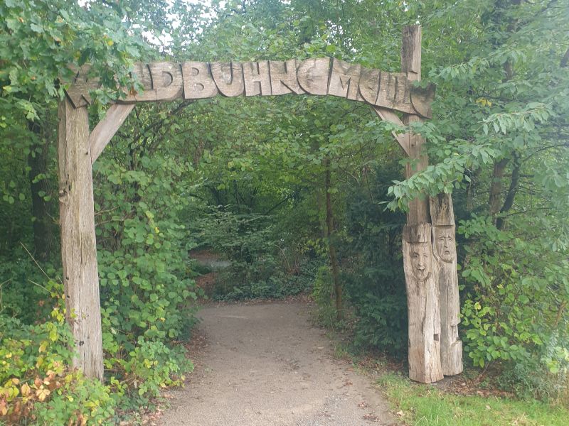 Ein hölzernes Tor an einem Waldweg, da steht "Waldbühne Melle".