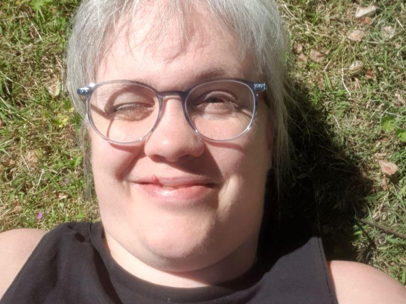 Paula liegt auf einer Wiese in der Sonne und kneift die Augen zu.