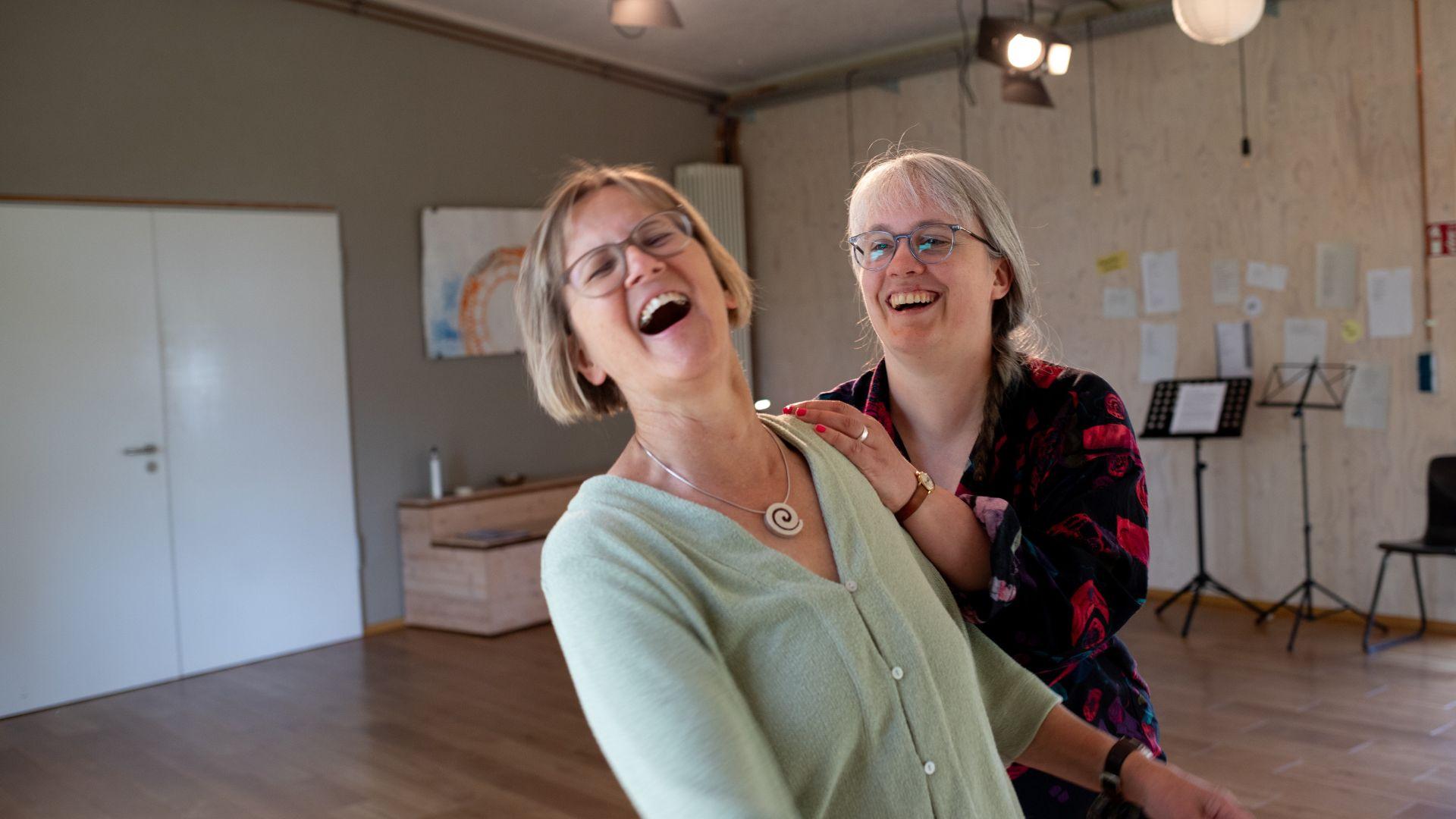 Paula legt einer Frau im Sprechtraining die Hand auf die Schulter. Beide lachen.