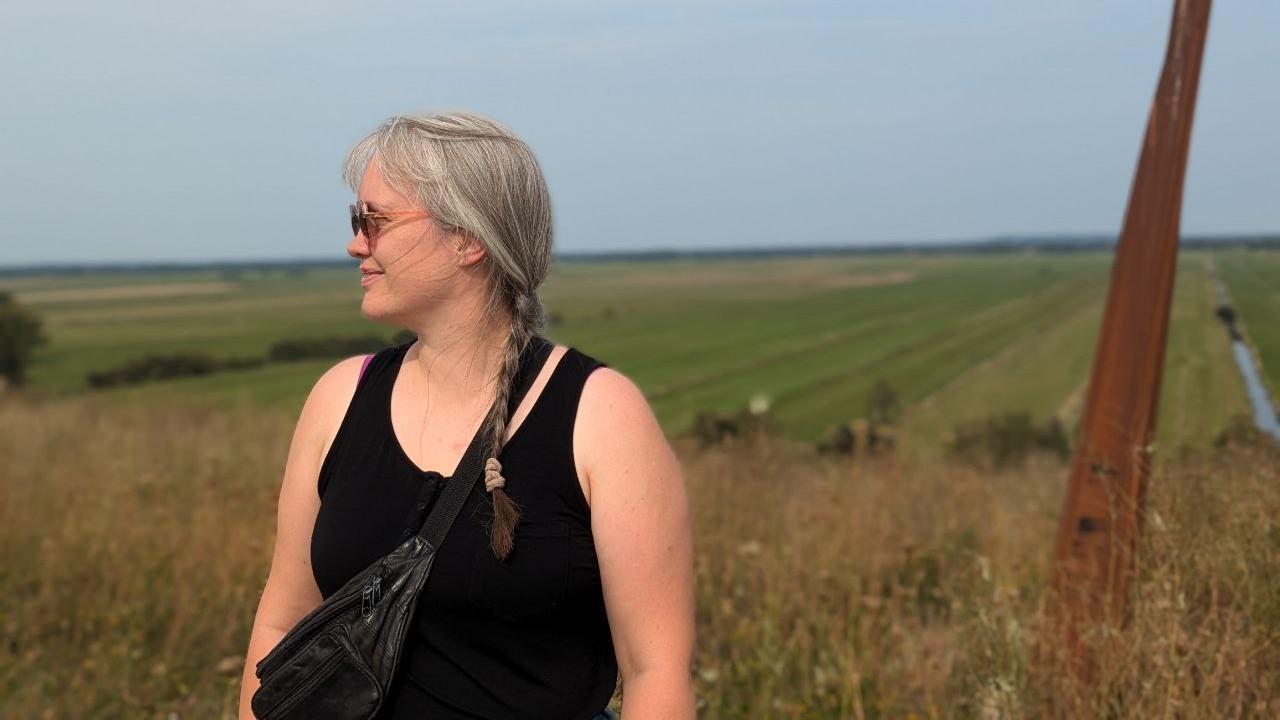 Paula steht vor einer weiten Landschaft und schaut nach links.