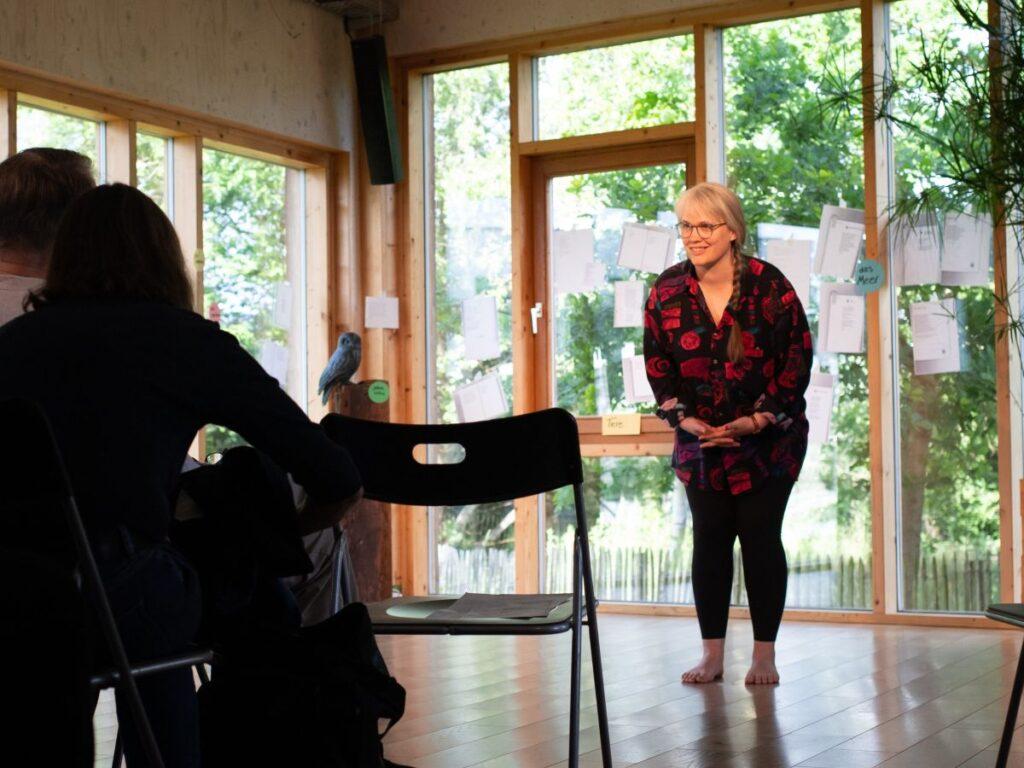 Paula steht in einem hellen Raum vor Publikum und verbeugt sich.