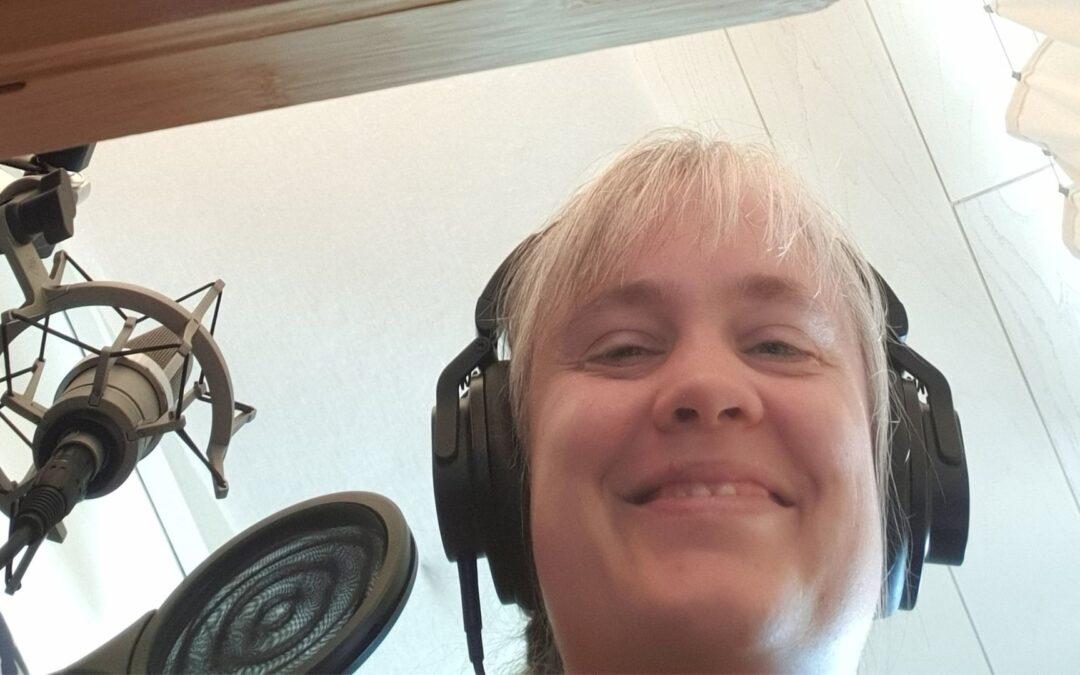 Paula schaut von oben ins Bild hinein. Sie hat Kopfhörer aus und neben ihr ist ein Mikrofon zu sehen.