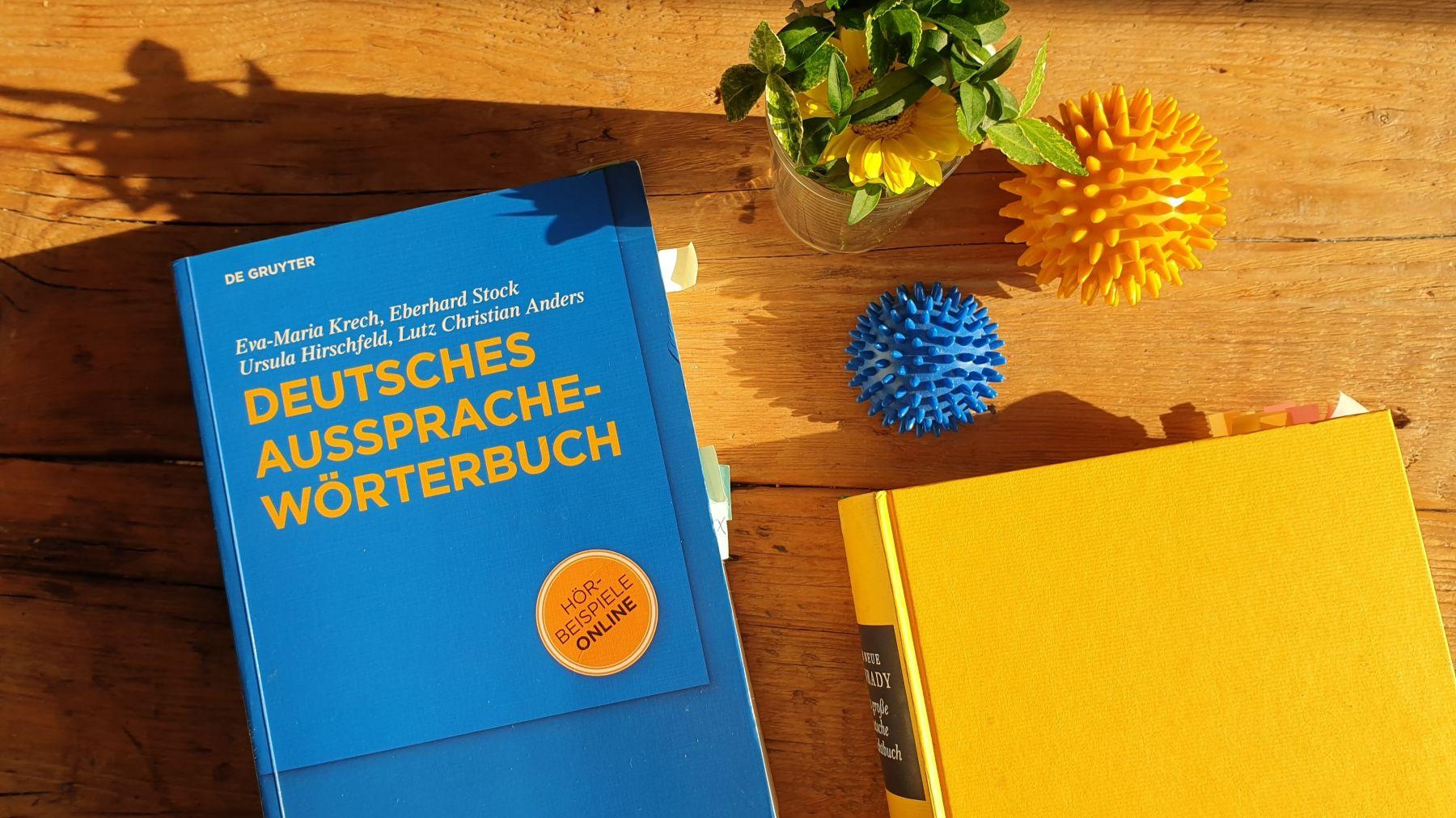 Zwei Bücher auf einem Tisch. Eines ist blau und trägt den Titel "Deutsches Aussprachewörterbuch". Das andere ist gelb und der Titel ist nicht sichtbar.