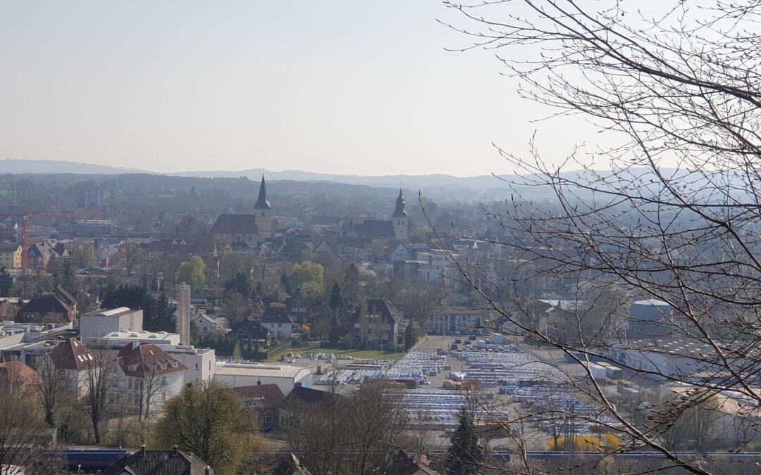 Ausblick auf eine kleine Stadt mit zwei Kirchtürmen. Im Hintergrund sind sanfte Berge in blauem Dunst.