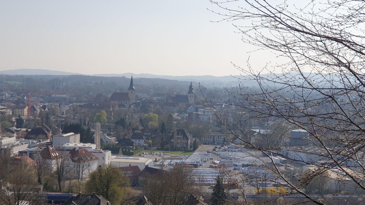 Ausblick auf eine kleine Stadt mit zwei Kirchtürmen. Im Hintergrund sind sanfte Berge in blauem Dunst.
